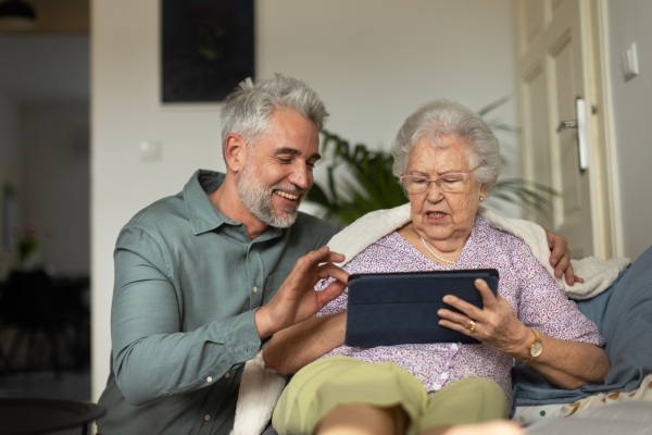 Mature man learning his senior mother working with a digital tablet.