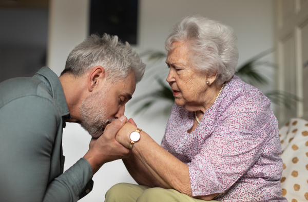 Portrait of mature man with his senior mother. Son kissing his mothers hands. Coping with grief, loss together.