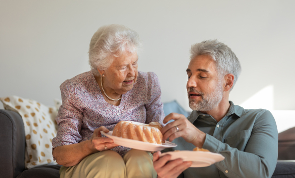 Portrait of senior mother giving her adult son fresh baked bundt cake.