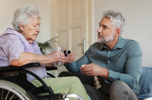 Close up of adult son giving pills to his ill mother. Taking prescribed medication. Helping senior take medication safely, at the right time.