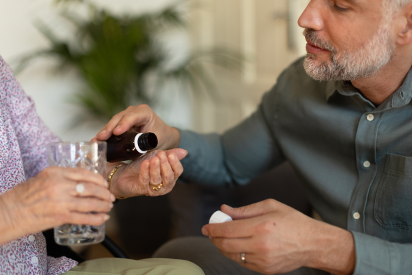 Close up of adult son giving pills to his ill mother. Taking prescribed medication. Helping senior take medication safely, at the right time.