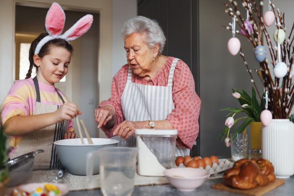 Grandmother with grandaughter preparing traditional easter meals, baking cakes and sweets. Passing down family recipes, custom and stories. Concept of family easter holidays.