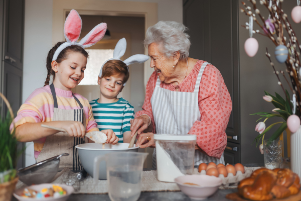 Grandmother with grandchildren preparing traditional easter meals, baking cakes and sweets. Passing down family recipes, custom and stories. Concept of family easter holidays.