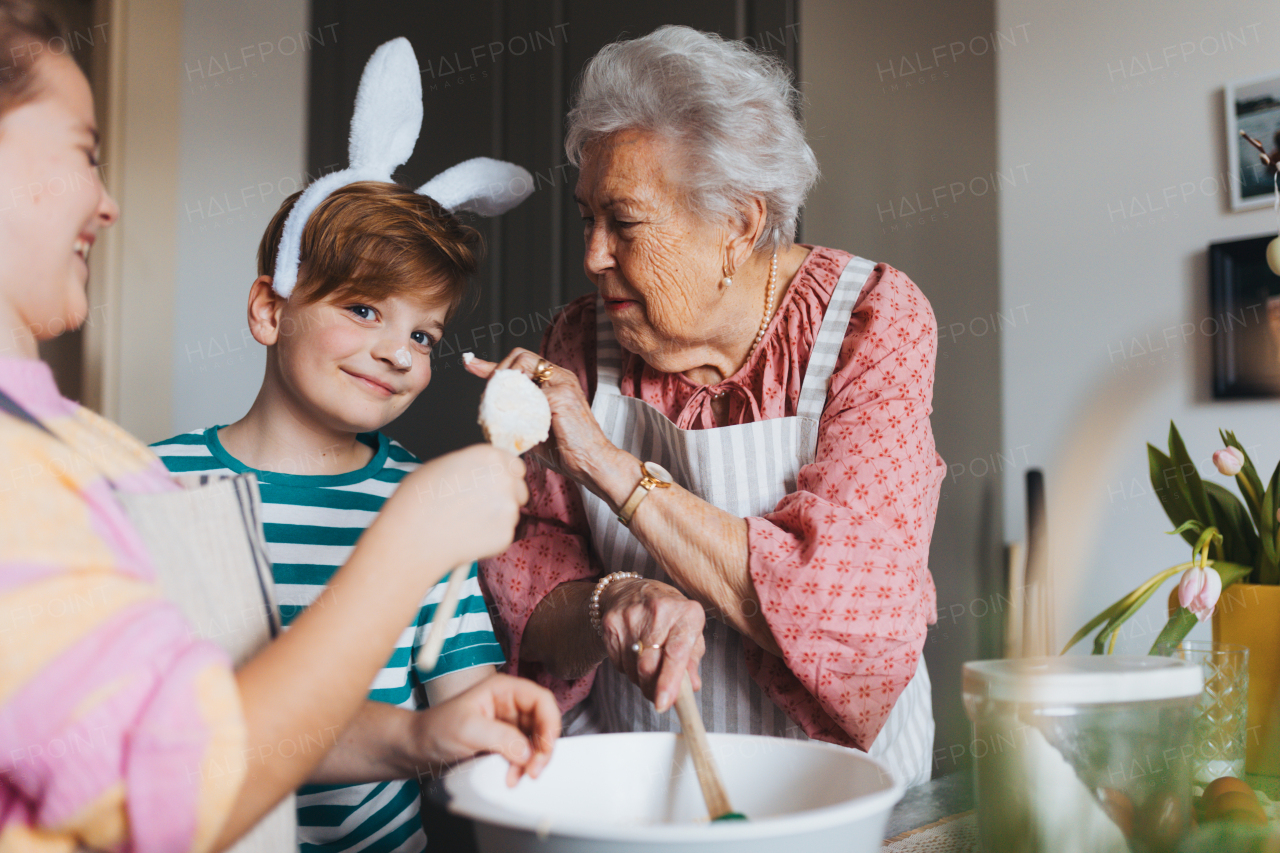 Grandmother with grandchildren baking cakes and sweets for easter, having fun. Boy with cake batter on nose. Passing down family recipes, custom and stories. Concept of family easter holidays.