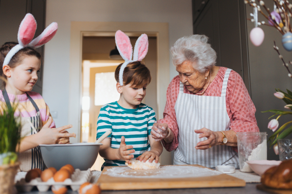 Grandmother with grandchildren preparing traditional easter meals, kneading dough for easter cross buns. Passing down family recipes, custom and stories. Concept of family easter holidays.