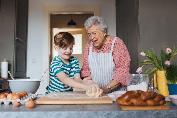 Grandmother with grandson preparing traditional easter meals, kneading dough for easter cross buns. Passing down family recipes, custom and stories. Concept of family easter holidays.