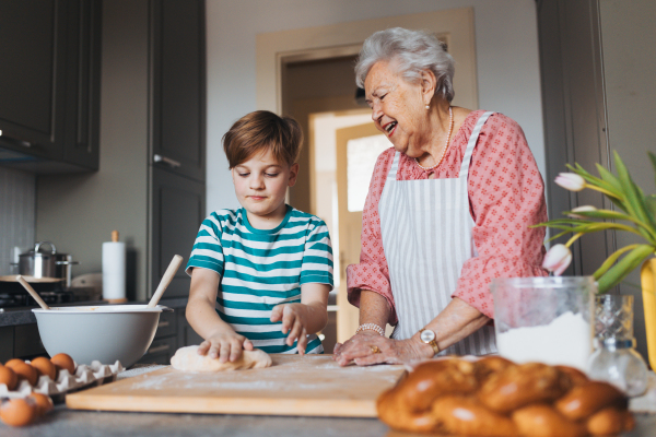 Grandmother with grandson preparing traditional easter meals, kneading dough for easter cross buns. Passing down family recipes, custom and stories. Concept of family easter holidays.