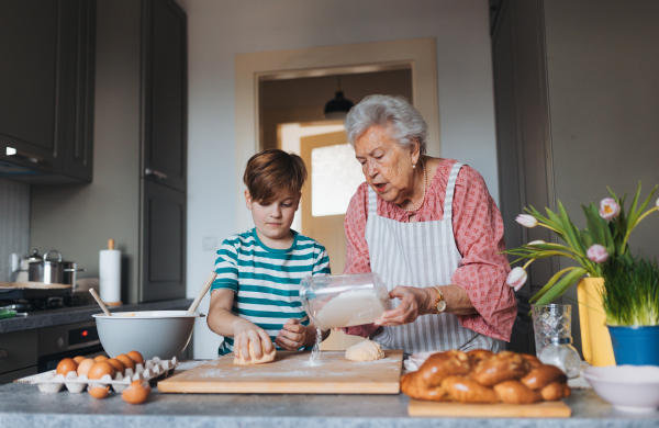 Grandmother with grandson preparing traditional easter meals, kneading dough for easter cross buns. Passing down family recipes, custom and stories. Concept of family easter holidays.