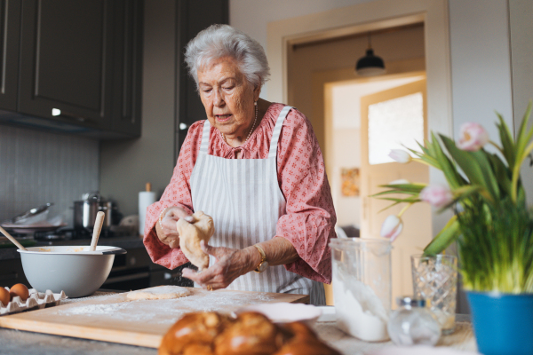 Senior woman preparing traditional easter meals for family, kneading dough for easter cross buns. Recreating family recipes, custom. Concept of easter holidays and traditions.