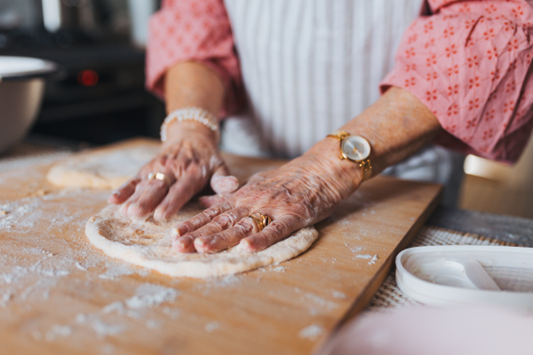 Close up of hands of senior woman preparing traditional easter meals for family, kneading dough for easter cross buns. Recreating family recipes, custom. Concept of easter holidays and traditions.