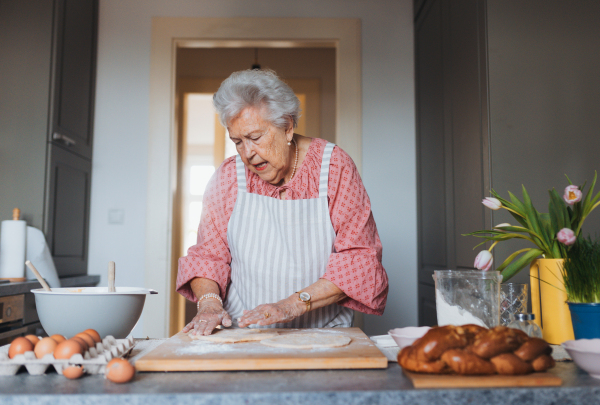 Senior woman preparing traditional easter meals for family, kneading dough for easter cross buns. Recreating family recipes, custom. Concept of easter holidays and traditions.