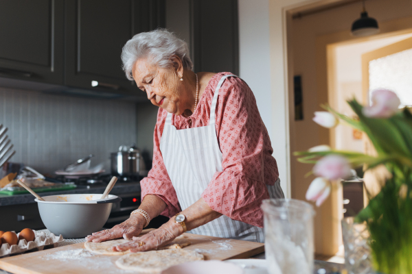 Senior woman preparing traditional easter meals for family, kneading dough for easter cross buns. Recreating family recipes, custom. Concept of easter holidays and traditions.