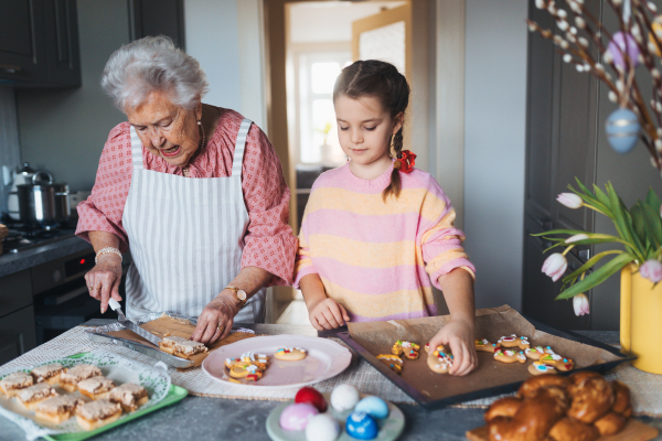 Grandmother with grandaughter preparing traditional easter meals, baking cakes and sweets. Passing down family recipes, custom and stories. Concept of family easter holidays.