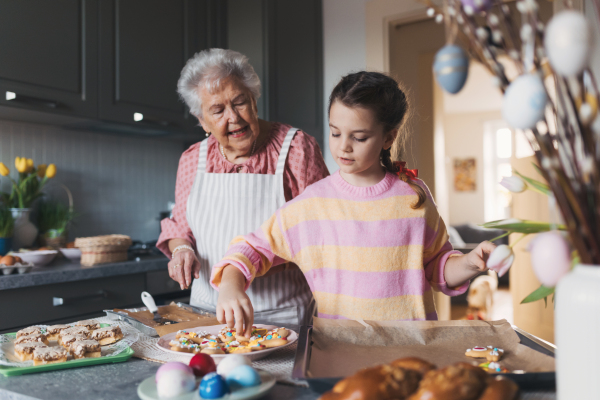 Grandmother with grandaughter preparing traditional easter meals, baking cakes and sweets. Passing down family recipes, custom and stories. Concept of family easter holidays.