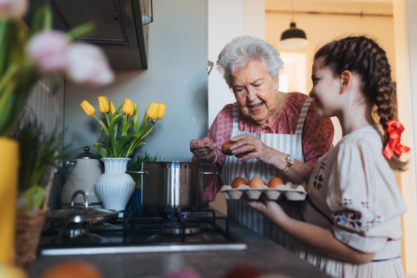 Grandmother with granddaughter preparing traditional easter meals, boiling eggs with natural dye to colour shells. Passing down family recipes, custom and stories. Concept of family easter holidays.