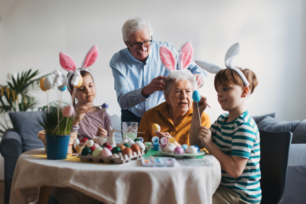 Grandmother with little kids decorating easter eggs at home. Tradition of painting eggs with brush and easter egg dye. Concept of family easter holidays.