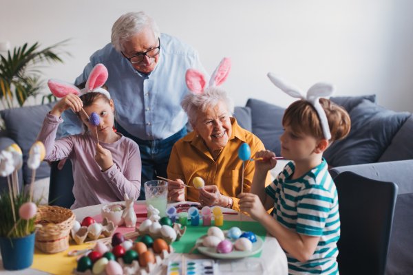 Grandmother with little kids decorating easter eggs at home. Tradition of painting eggs with brush and easter egg dye. Concept of family easter holidays.