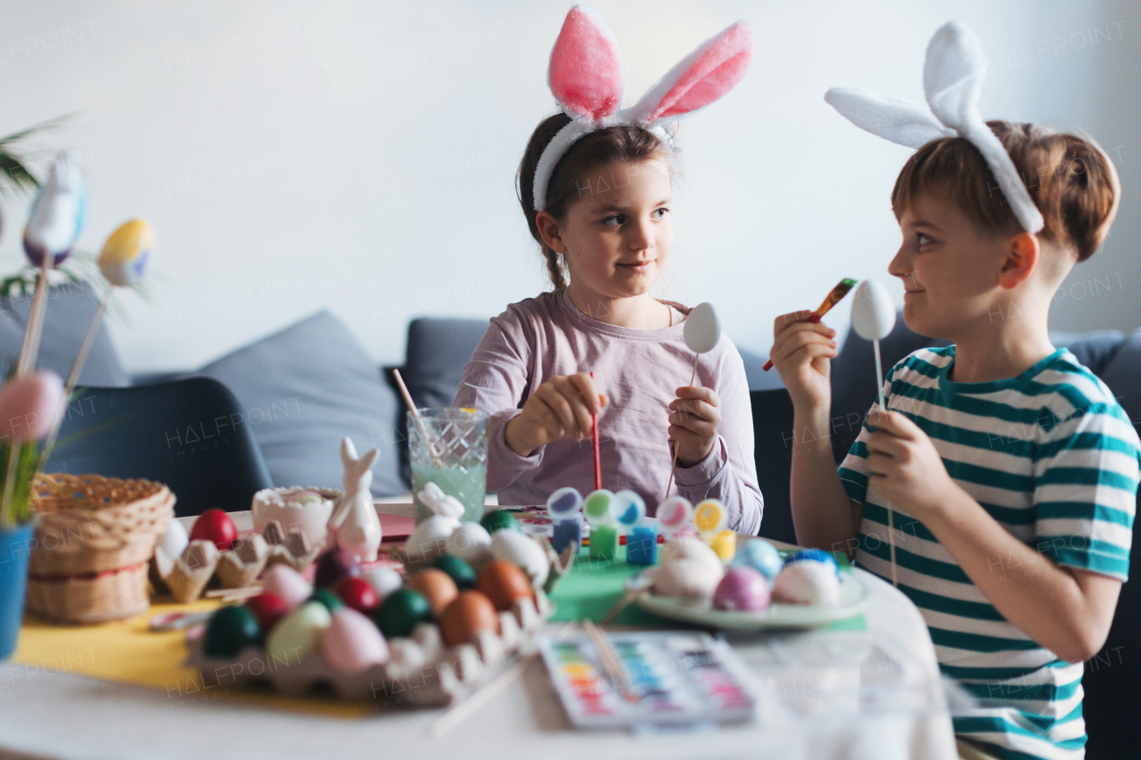 Two kids, siblings decorating easter eggs at home. Tradition of painting eggs with brush and easter egg dye. Concept of family easter holidays.