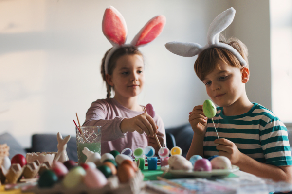 Two kids, siblings decorating easter eggs at home. Tradition of painting eggs with brush and easter egg dye. Concept of family easter holidays.