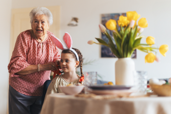 Grandmother braiding granddaughter's hair, putting red ribbon on braid. Prepairing for easter lunch.. Concept of family easter holidays.