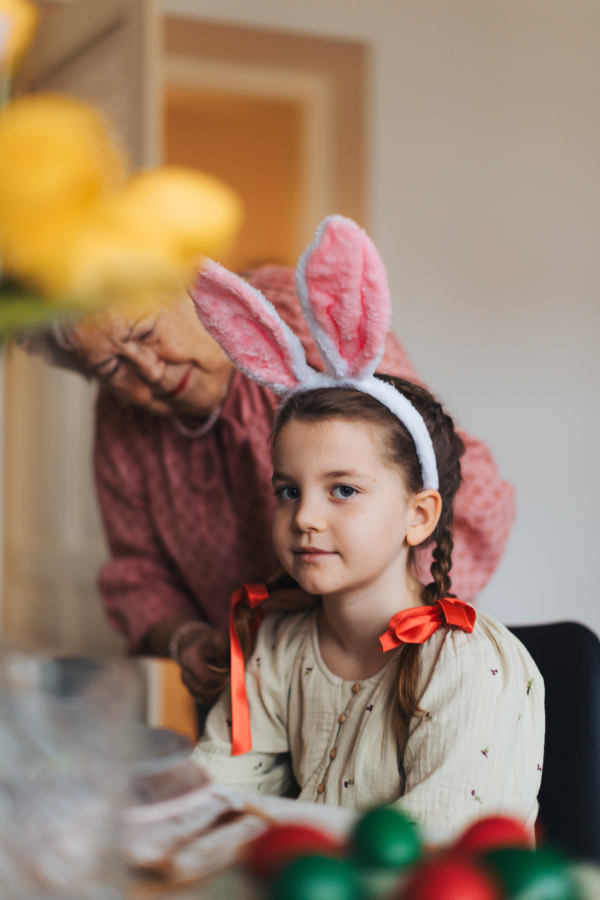 Grandmother braiding hair of granddaughter, putting ribbon ob braid. Prepairing for easter lunch.. Concept of family easter holidays.