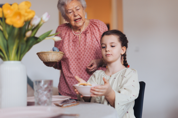 Grandmother with granddaughter setting table for traditional easter lunch. Recreating family traditions and customs. Concept of family easter holidays. Standing by table, praying.