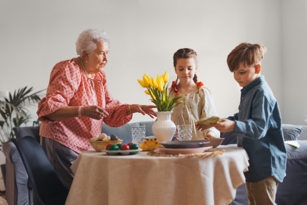 Grandmother with grandchildren setting table for traditional easter lunch. Recreating family traditions and customs. Concept of family easter holidays.