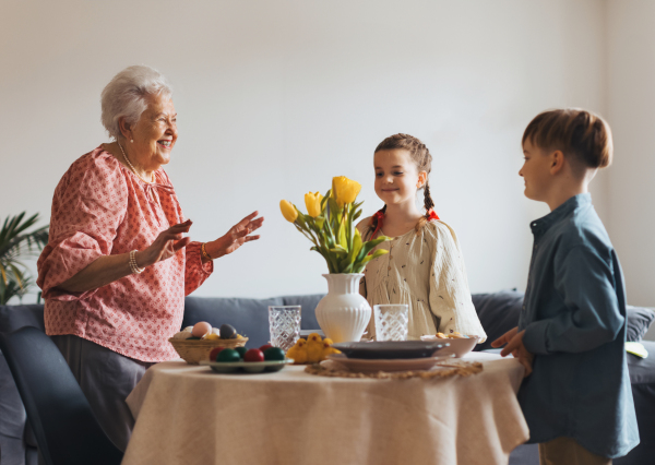 Grandmother with grandchildren setting table for traditional easter lunch. Recreating family traditions and customs. Concept of family easter holidays. Standing by table, praying.