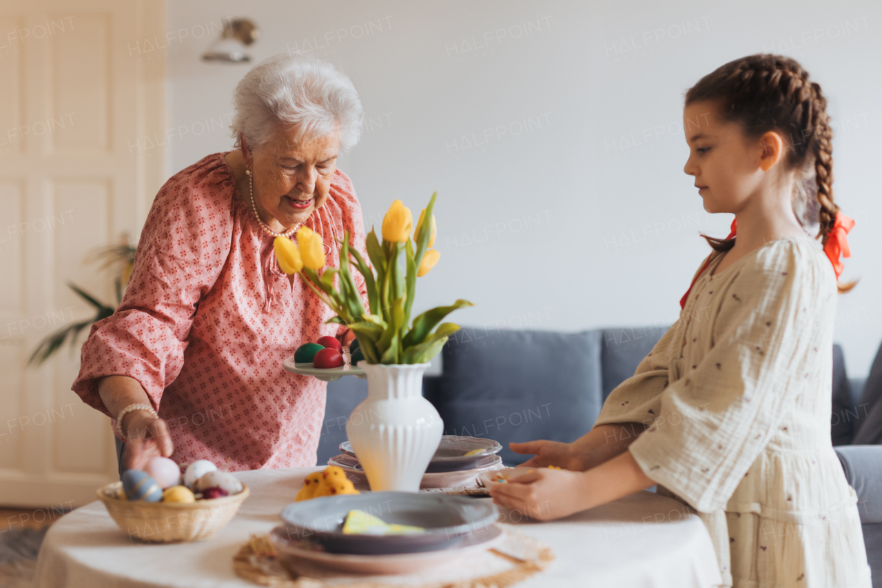 Grandmother with granddaughter setting table for traditional easter lunch. Recreating family traditions and customs. Concept of family easter holidays. Standing by table, praying.