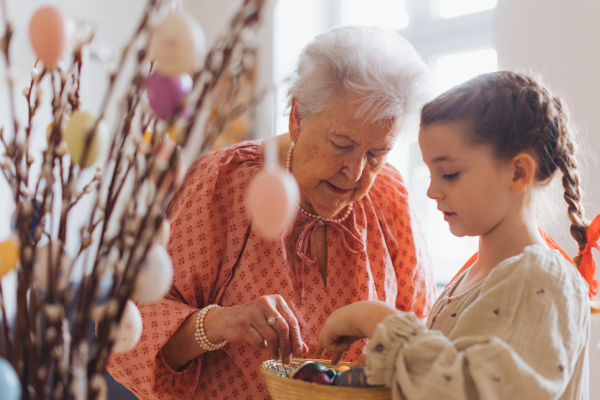 Grandmother with grandaughter decorating pussy willows branches, putting easter eggs on them. Concept of family easter holidays.