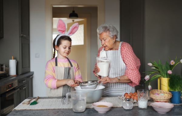 Grandmother with grandaughter preparing traditional easter meals, baking cakes and sweets. Passing down family recipes, custom and stories. Concept of family easter holidays.