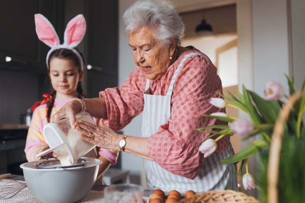 Grandmother with granddaughter preparing traditional easter meals, baking cakes and sweets. Passing down family recipes, custom and stories. Concept of family easter holidays.