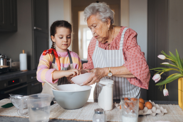 Grandmother with grandaughter preparing traditional easter meals, baking cakes and sweets. Passing down family recipes, custom and stories. Concept of family easter holidays.