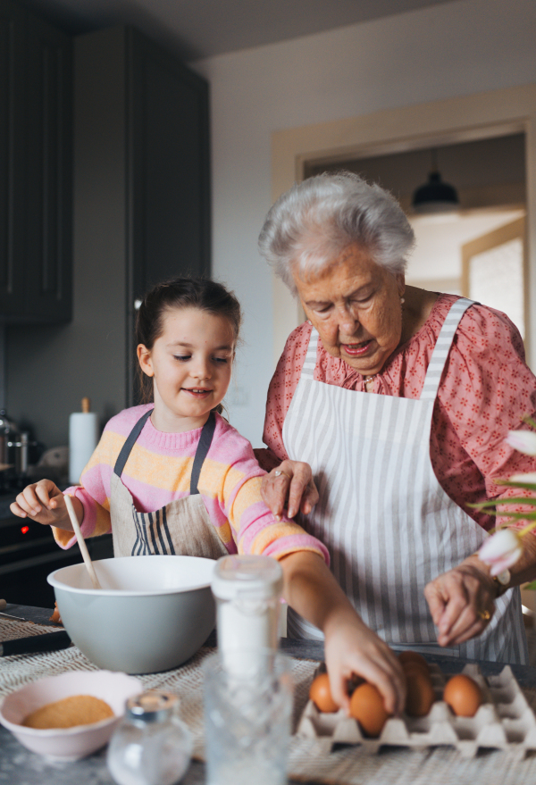 Grandmother with granddaughter preparing traditional easter meals, baking cakes and sweets. Passing down family recipes, custom and stories. Concept of family easter holidays.