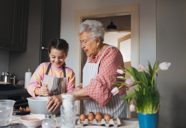 Grandmother with grandaughter preparing traditional easter meals, baking cakes and sweets. Passing down family recipes, custom and stories. Concept of family easter holidays.