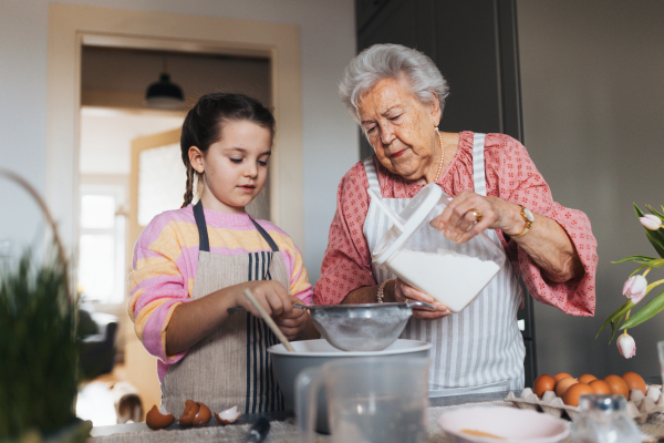 Grandmother with granddaughter preparing traditional easter meals, baking cakes and sweets. Passing down family recipes, custom and stories. Concept of family easter holidays.