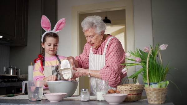 Grandmother with grandaughter preparing traditional easter meals, baking cakes and sweets. Passing down family recipes, custom and stories. Concept of family easter holidays.