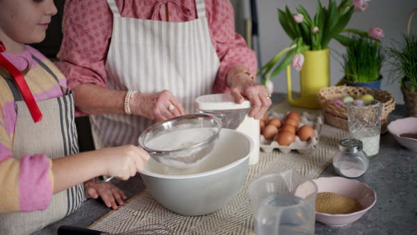 Grandmother with grandaughter preparing traditional easter meals, baking cakes and sweets. Passing down family recipes, custom and stories. Concept of family easter holidays.