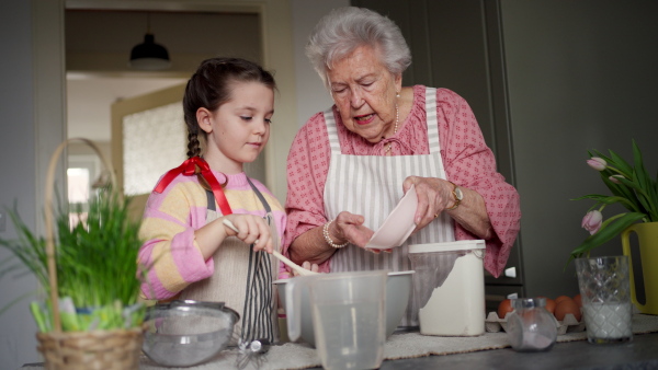 Grandmother with grandaughter preparing traditional easter meals, baking cakes and sweets. Passing down family recipes, custom and stories. Concept of family easter holidays.