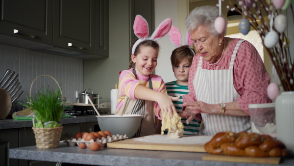 Grandmother with grandchildren preparing traditional easter meals, kneading dough for easter cross buns. Passing down family recipes, custom and stories. Concept of family easter holidays.