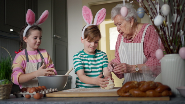 Grandmother with grandchildren preparing traditional easter meals, kneading dough for easter cross buns. Passing down family recipes, custom and stories. Concept of family easter holidays.