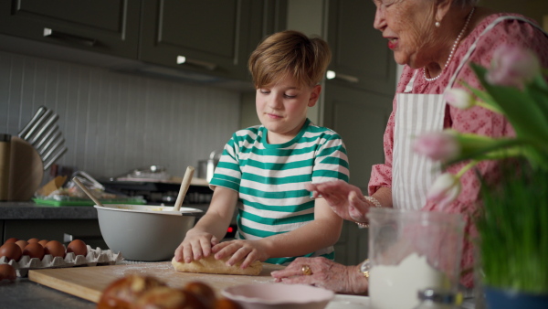 Grandmother with grandson preparing traditional easter meals, kneading dough for easter cross buns. Passing down family recipes, custom and stories. Concept of family easter holidays.