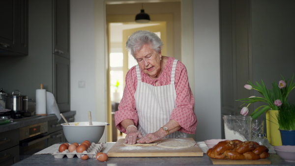 Senior woman preparing traditional easter meals for family, kneading dough for easter cross buns. Recreating family recipes, custom. Concept of easter holidays and traditions.