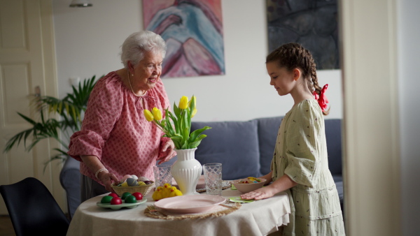 Grandmother with granddaughter setting table for traditional easter lunch. Recreating family traditions and customs. Concept of family easter holidays. Standing by table, praying.