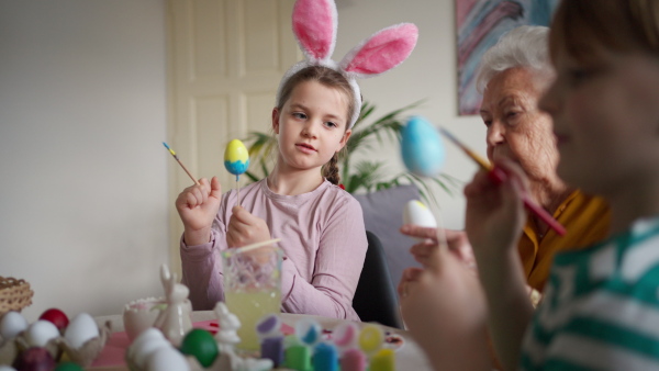 Grandmother with little kids decorating easter eggs at home. Tradition of painting eggs with brush and easter egg dye. Concept of family easter holidays.