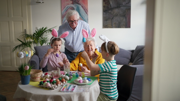 Grandmother with little kids decorating easter eggs at home. Tradition of painting eggs with brush and easter egg dye. Concept of family easter holidays.