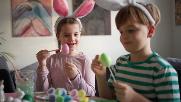 Two kids, siblings decorating easter eggs at home. Tradition of painting eggs with brush and easter egg dye. Concept of family easter holidays.