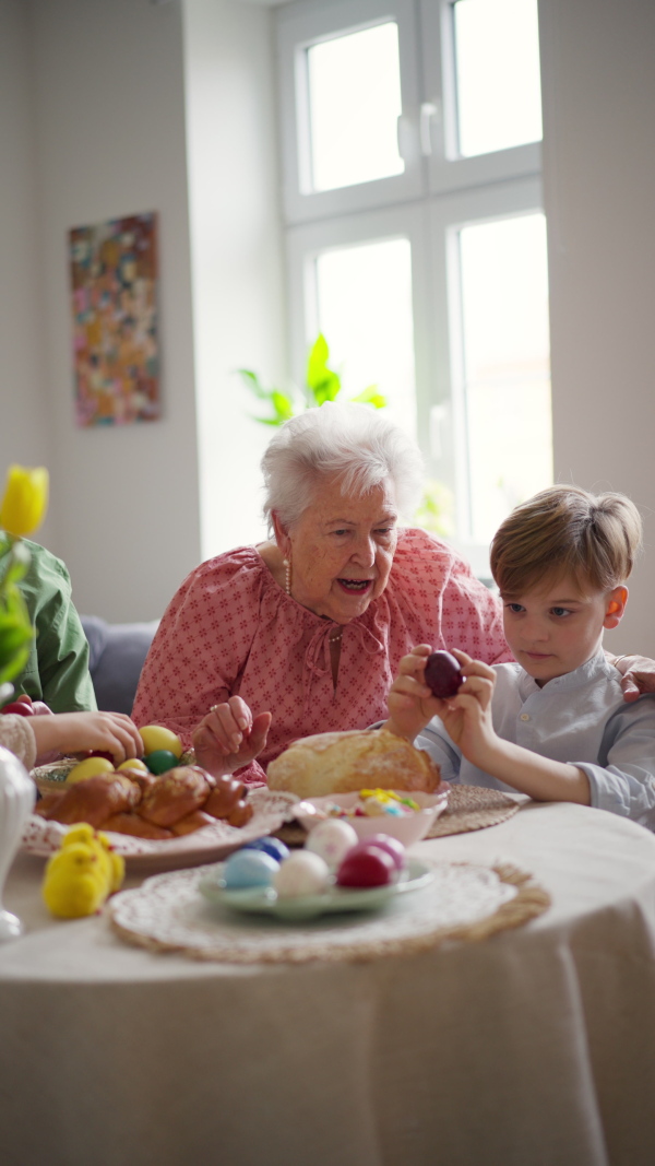 Grandmother with little kids decorating easter eggs at home. Tradition of painting eggs with brush and easter egg dye. Concept of family easter holidays.