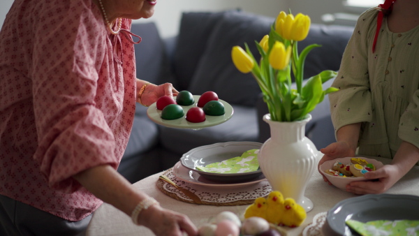 Grandmother with granddaughter setting table for traditional easter lunch. Recreating family traditions and customs. Concept of family easter holidays. Standing by table, praying.