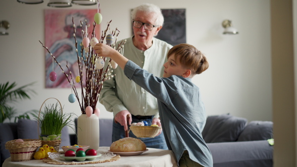 Grandfather with grandson setting table for traditional easter lunch. Recreating family traditions and customs. Concept of family easter holidays. Standing by table, praying.